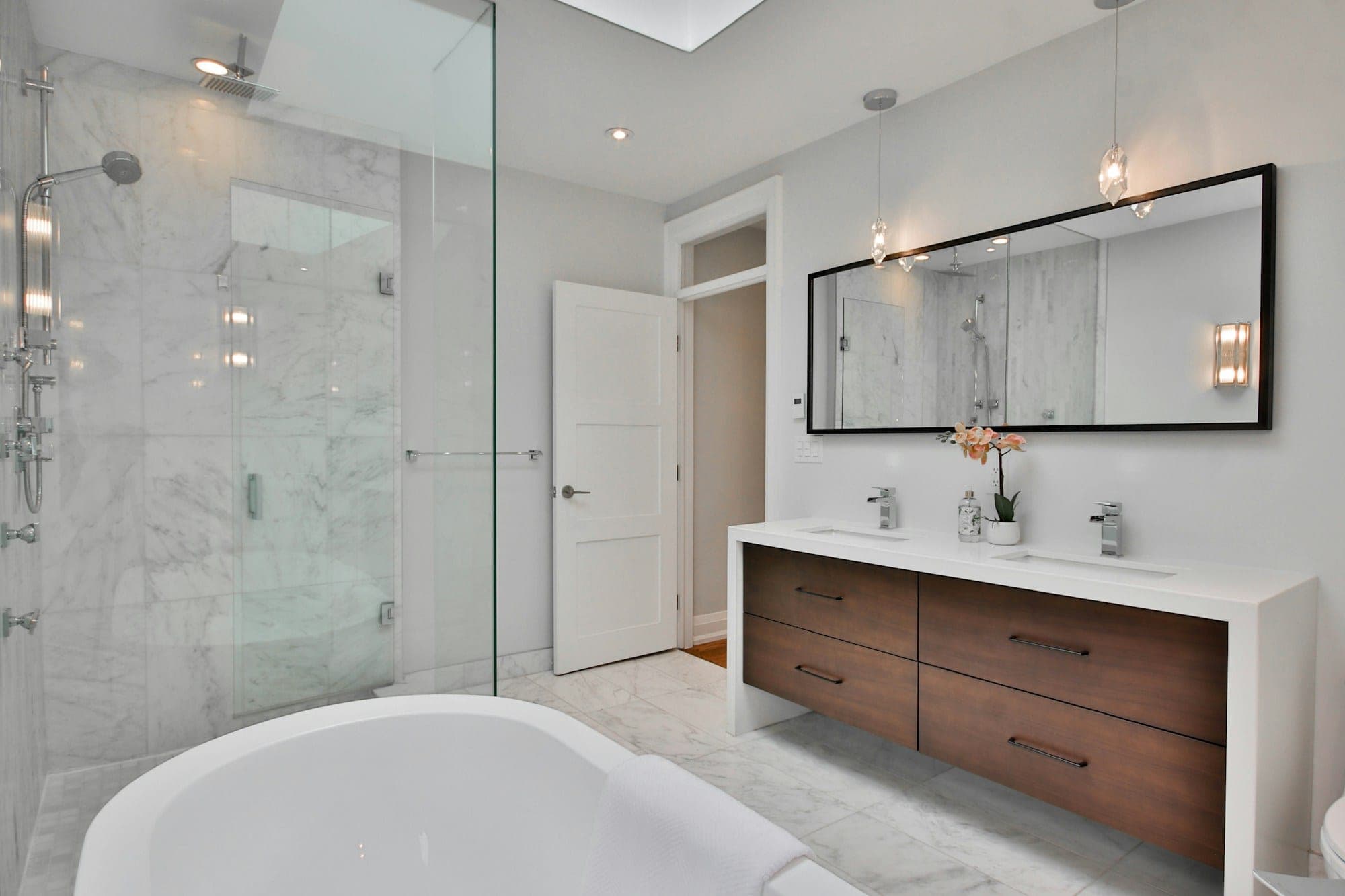 Bright bathroom with a floating wood vanity, marble walk-in shower and a soaking tub