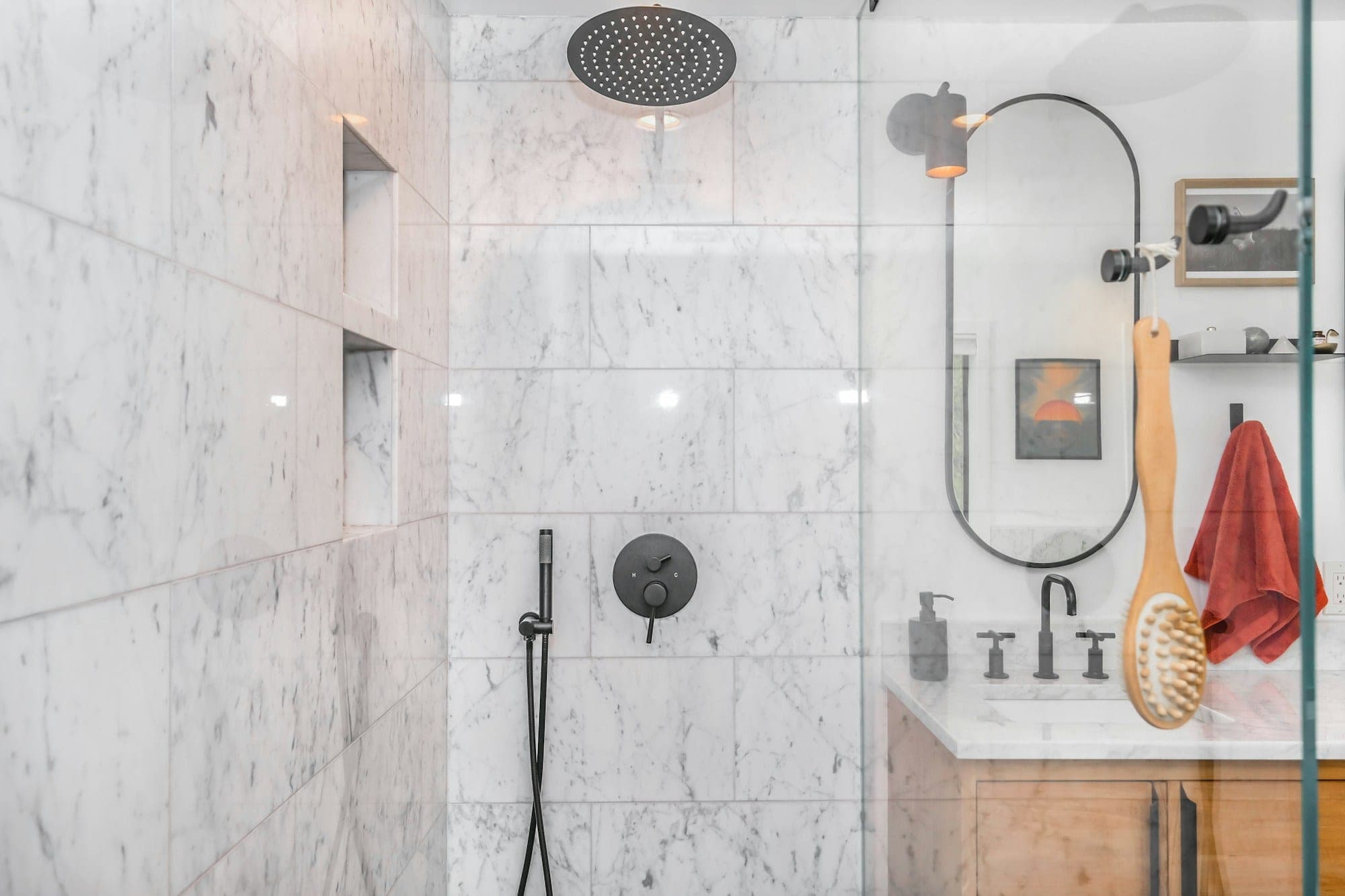 Marble-tiled shower with recessed niches and black fixtures beside a wood vanity