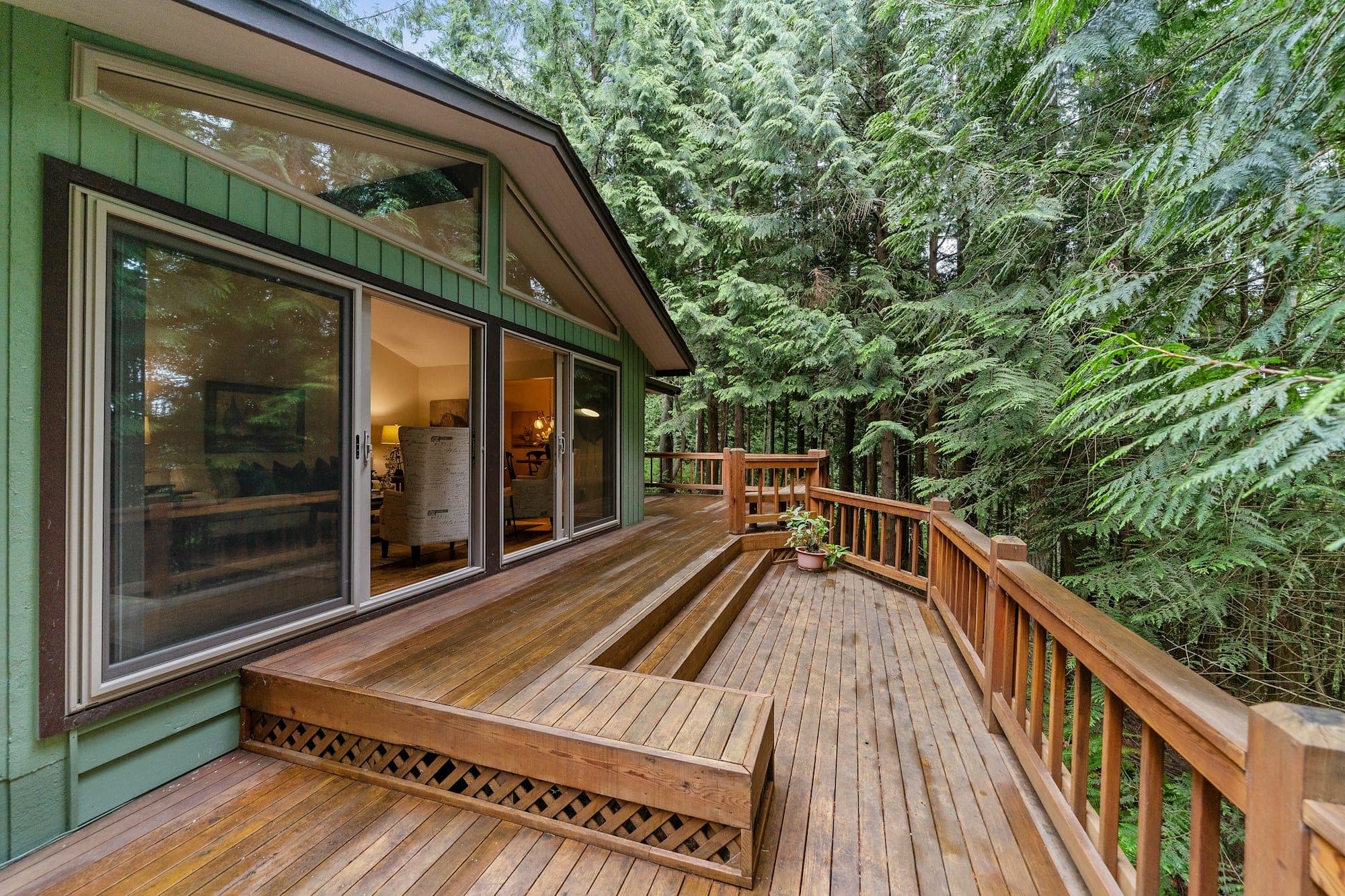 Wood deck with built-in bench steps and wood railing surrounded by evergreen trees