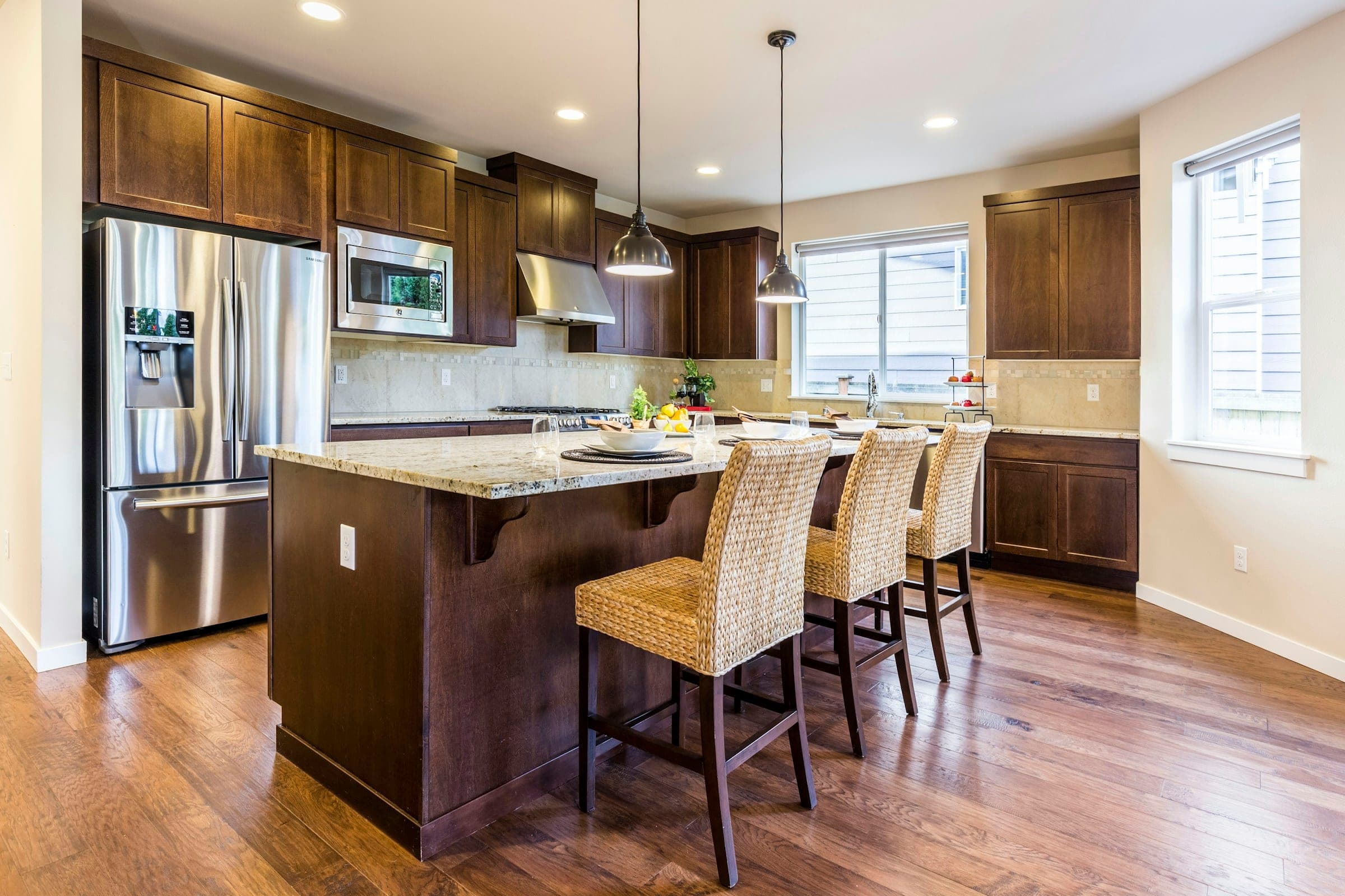 Kitchen with dark stained wood cabinetry, a stone-topped island with woven stools and pendant lights over hardwood floors