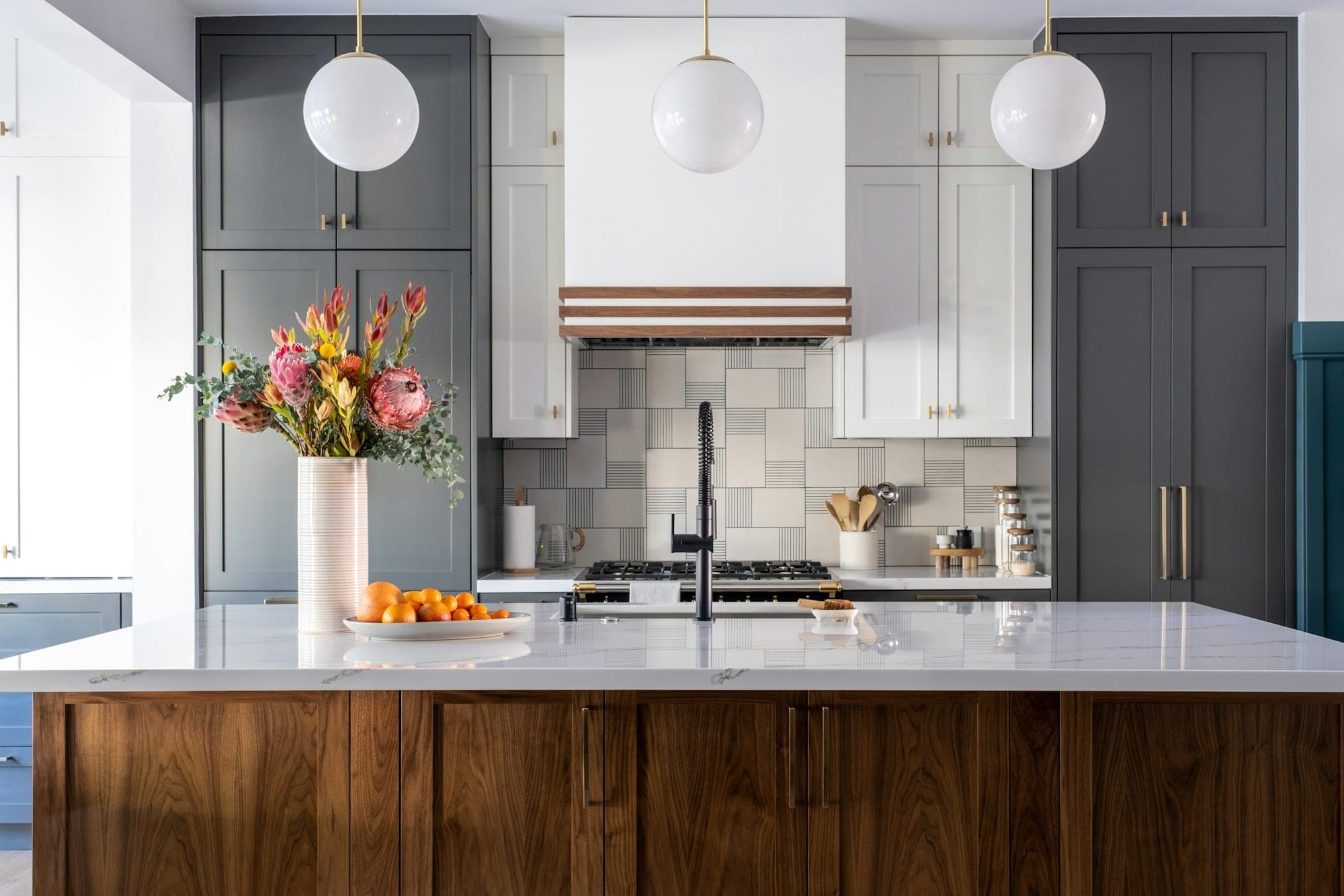Kitchen island with walnut cabinet fronts and a white quartz top beneath globe pendants
