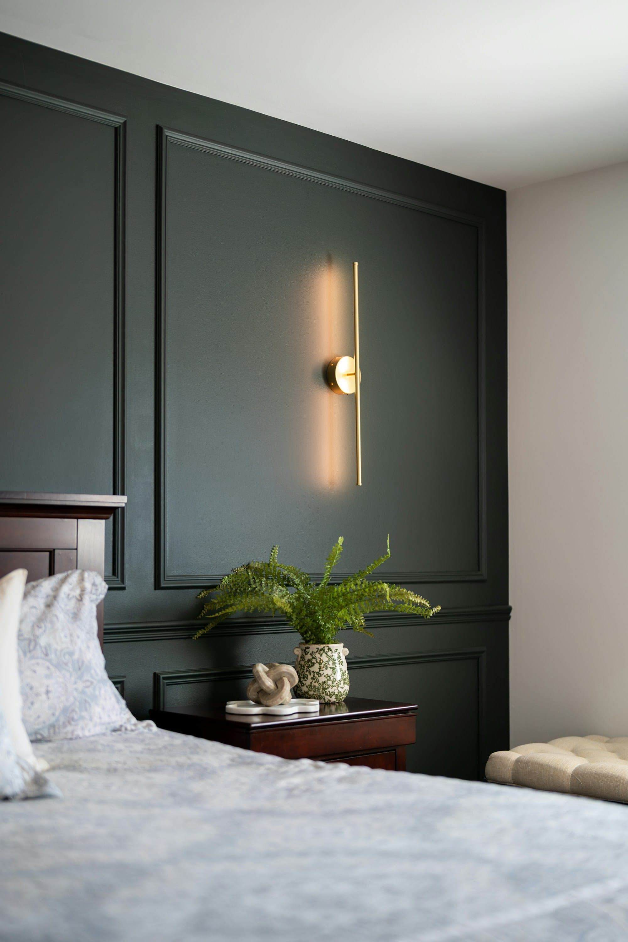 Deep green paneled wall with applied molding and a slim brass sconce