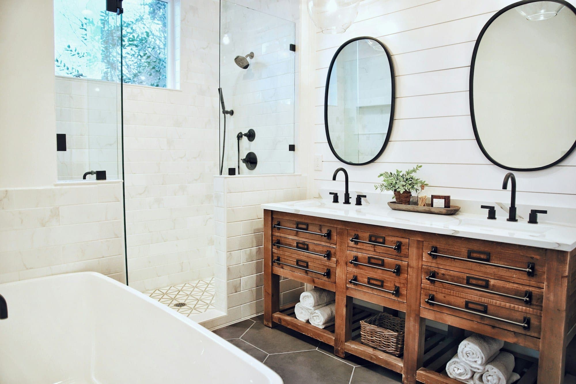 Bathroom with a wood double vanity, shiplap wall, oval mirrors and a freestanding tub