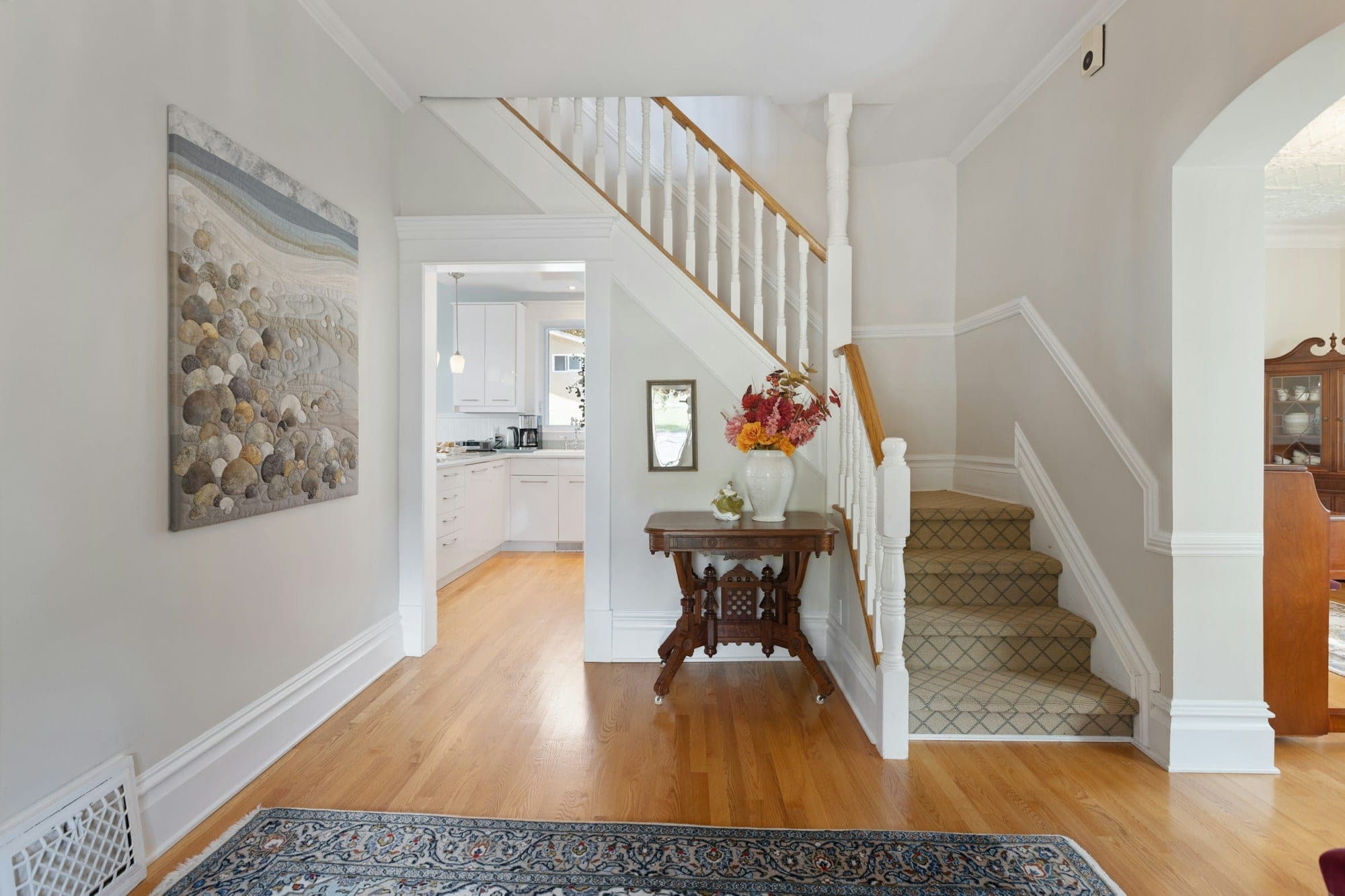 Front hall with a carpeted staircase, white balusters and a stained handrail over hardwood floors